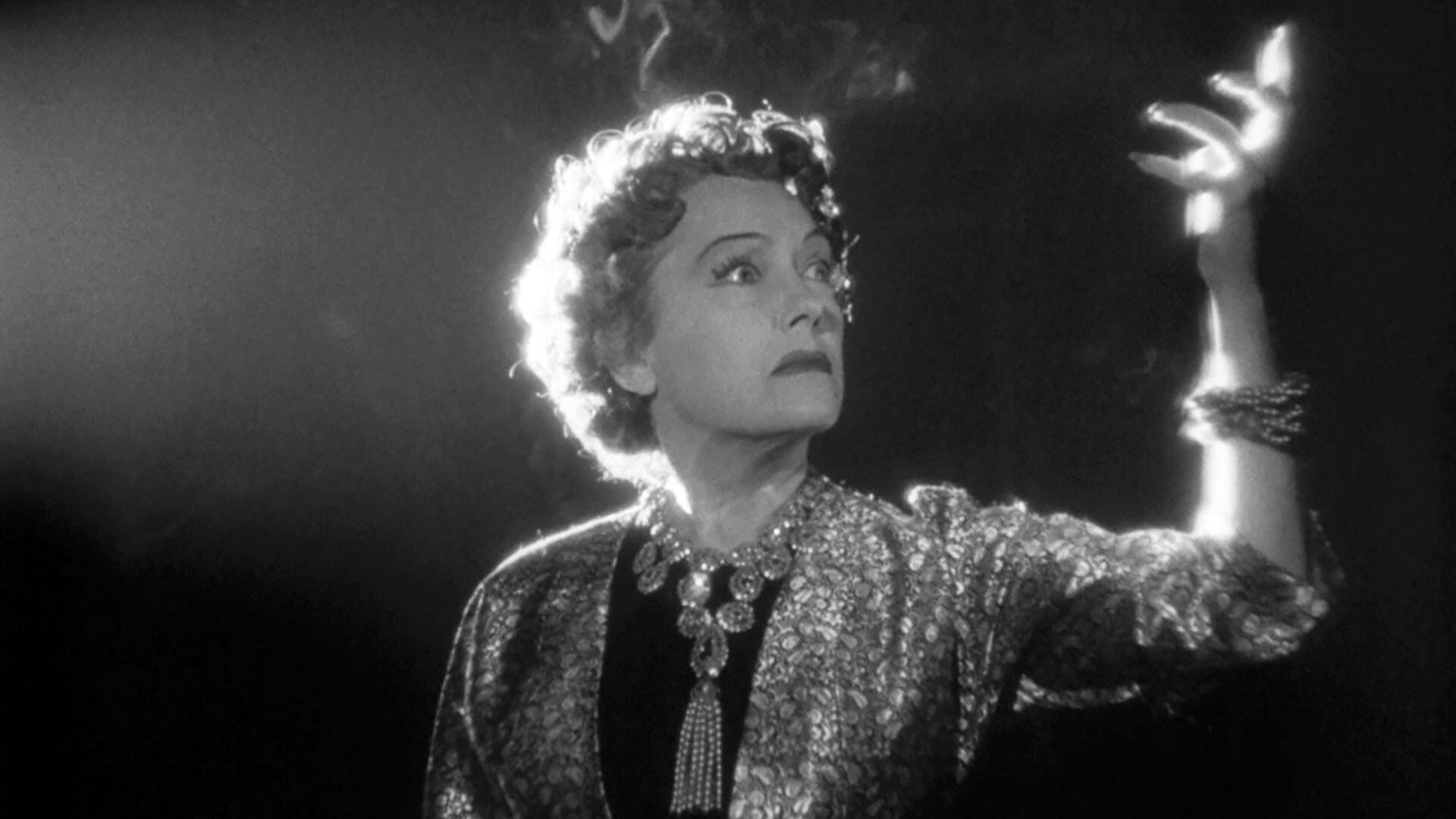 A mid-century film set imagined in warm sepia, a comic performer standing beside a director under studio lights, technicians adjusting equipment, bustling yet focused mood, painterly style