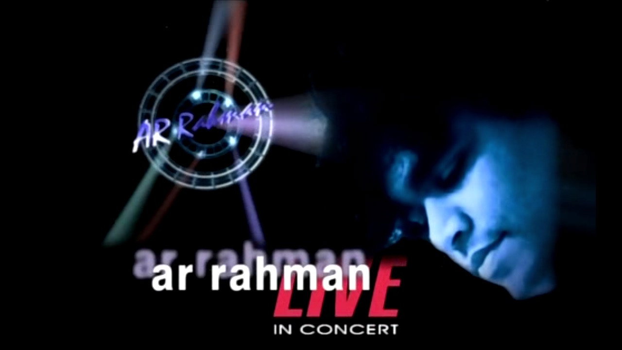 A film composer seated at a studio mixing console, headphones around his neck, sheet music and a tanpura beside him, warm lamplight falling across the keys of a keyboard, calm and workmanlike mood, cinematic wide shot